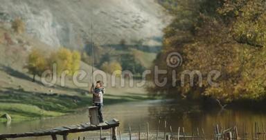 一个可爱的小男孩拿着一根<strong>大鱼</strong>竿在湖边的一座桥上玩。
